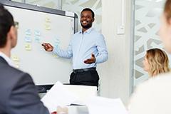 Man smiling pointing to white board while people look on.